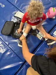 A toddler on a blue gym mat with stimulation units, with a therapist's hands guiding the session
